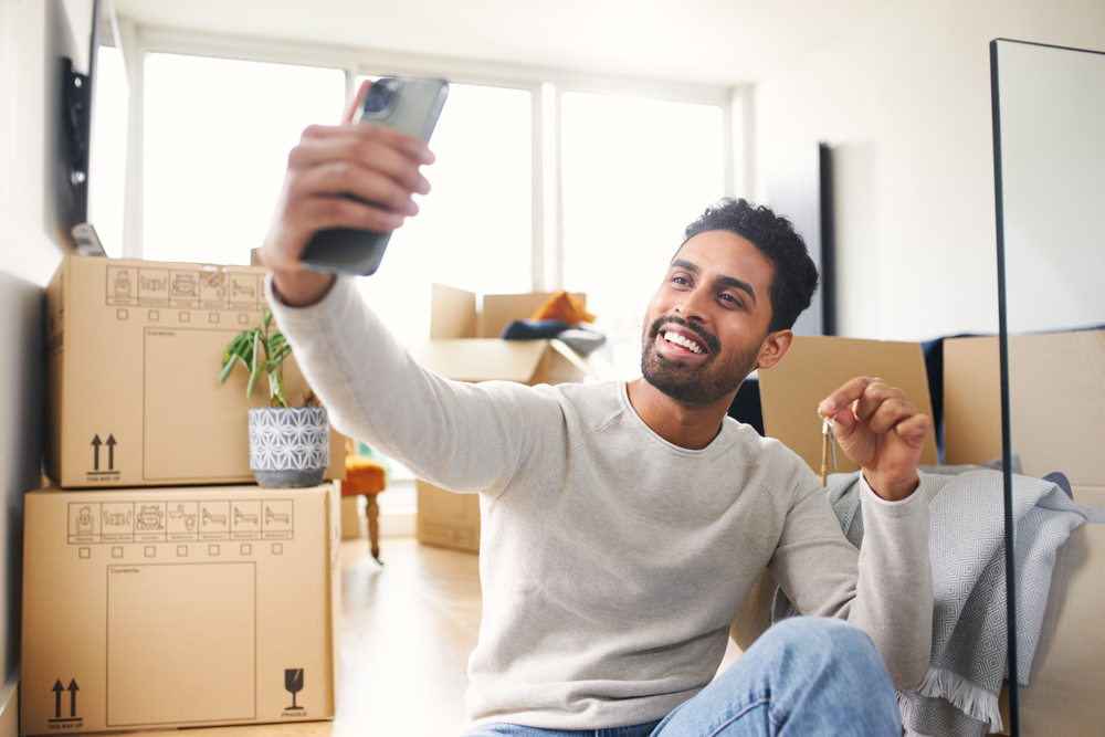 man smiling taking selfie in new apartment with boxes