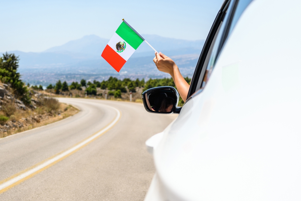 car driving down highway holding mexico flag out of the window